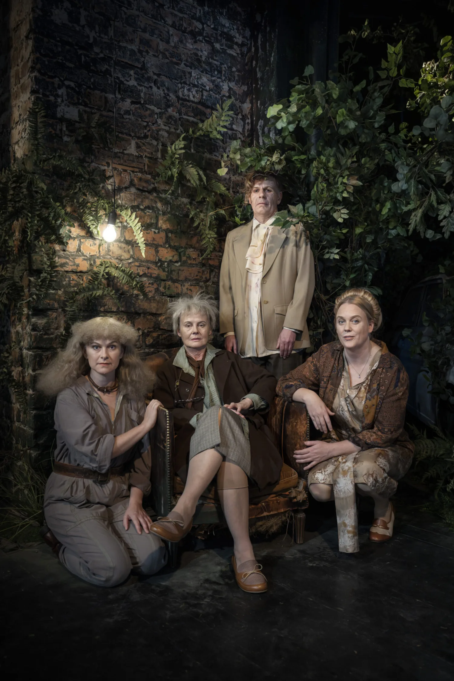 Bild på tre personer som sitter och en som står i mörker framför tegelvägg med lampa på.