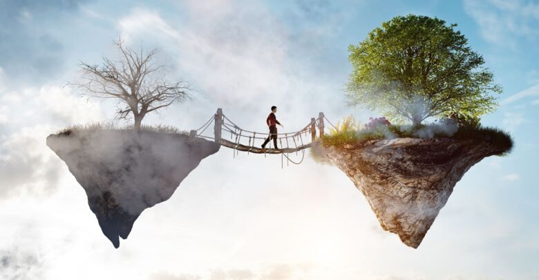 Bild på en person som går på en hängbro från en ö med ett dött träd mot en likadan ö med levande natur.
