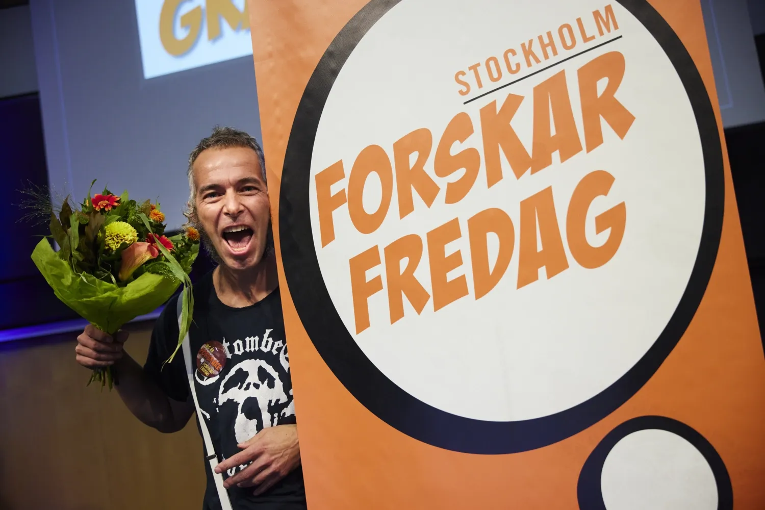 Erik Andersson bredvid en skylt för Forskar Fredag och med en blombukett i handen