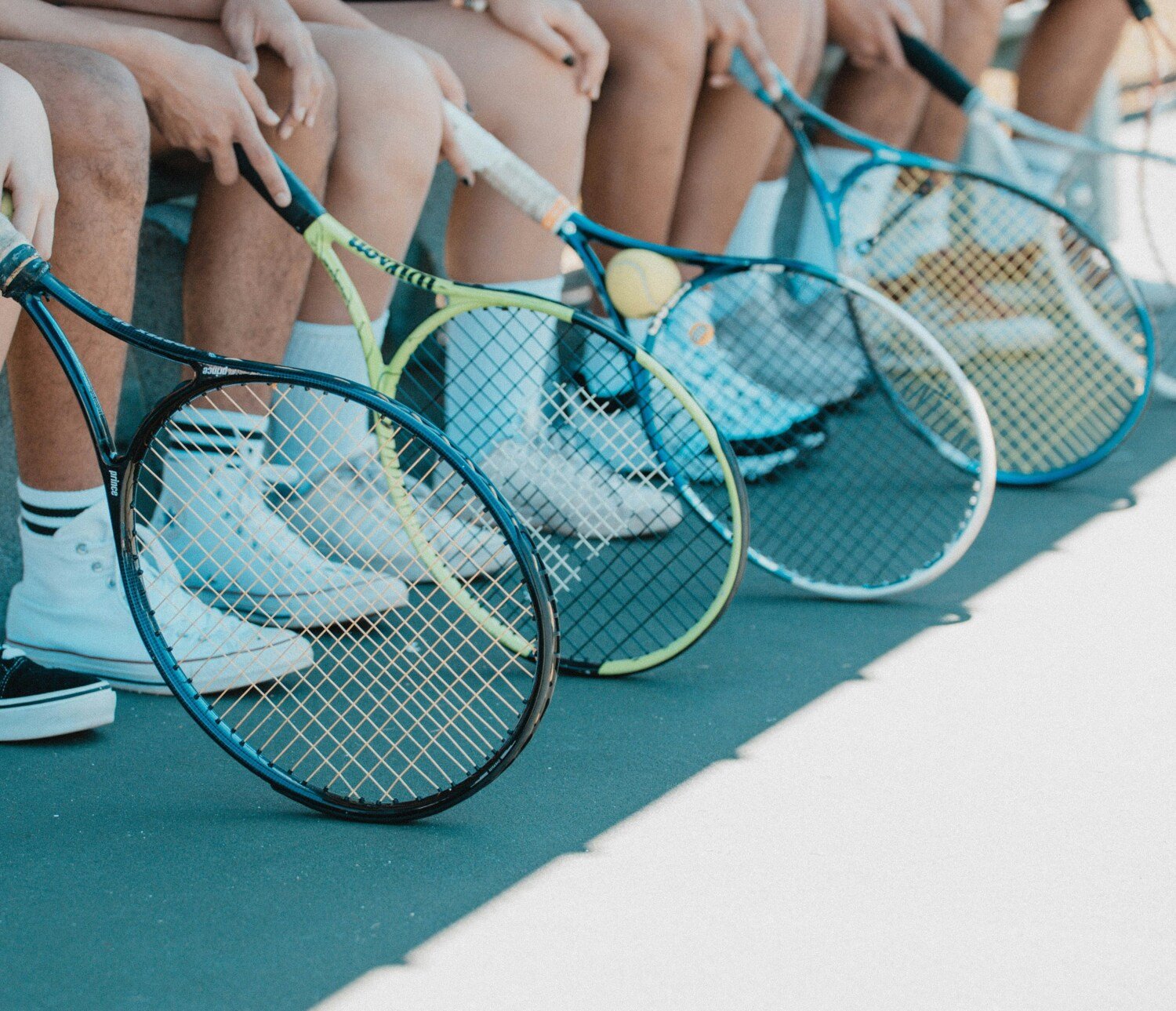 Flera personer som sitter på rad med ett varsitt tennisracket framför sig.