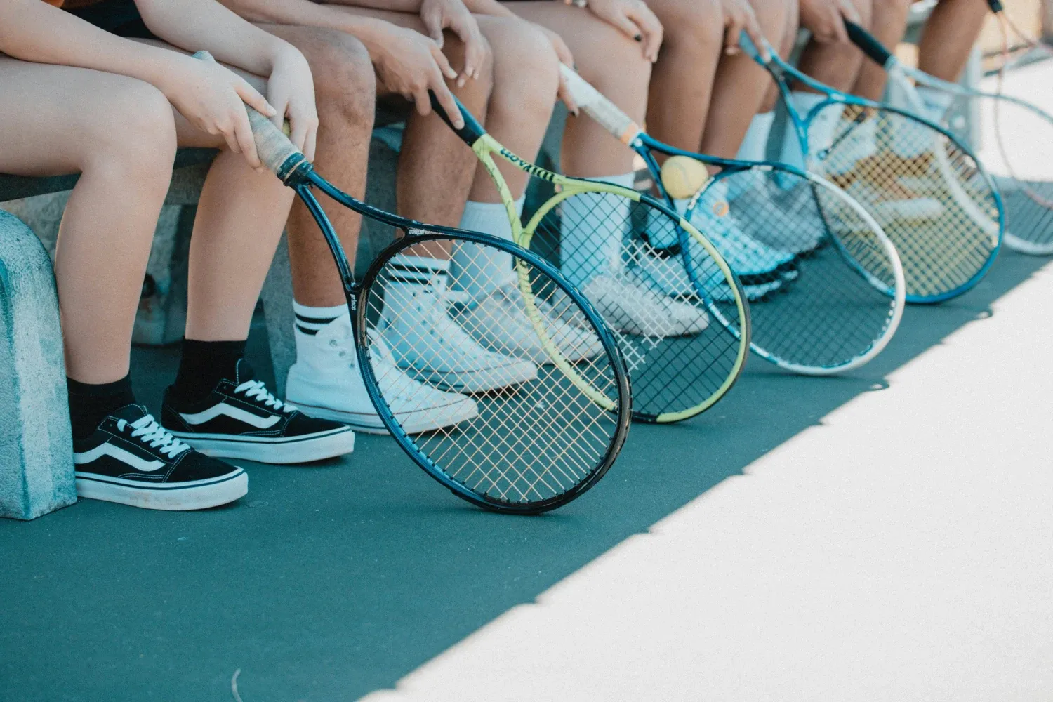 Flera personer som sitter på rad med ett varsitt tennisracket framför sig.