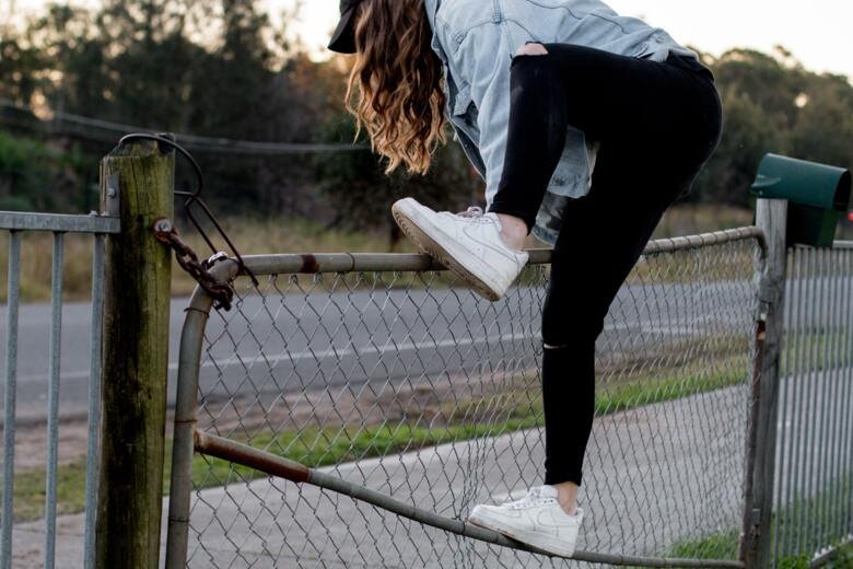 Ung kvinna klättrar över staket