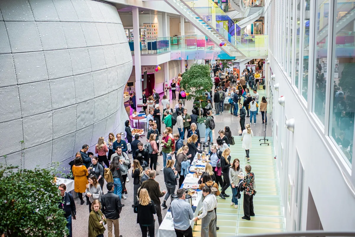 Översiktsbild från byggnaden Neo under konferensen. Personer står i öppen yta och minglar.