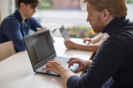 Student som sitter och pluggar med sin dator vid fönstret tillsammans med andra