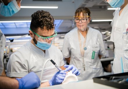Dental student examining a dummy, supervisors in the background.