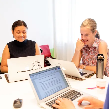 Studenter som arbetar tillsammans runt ett bord med sina datorer.
