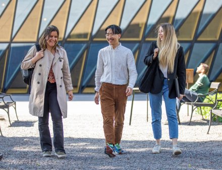 Studenter utomhus på campus Solna en solig vårdag 2022. || Studenter utanför Aula medica || Tre studenter går från campus. Aula medica syns i bakgrunden.