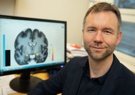 Porträtt av Andreas Olsson framför en bildskärm med en hjärna avbildad.